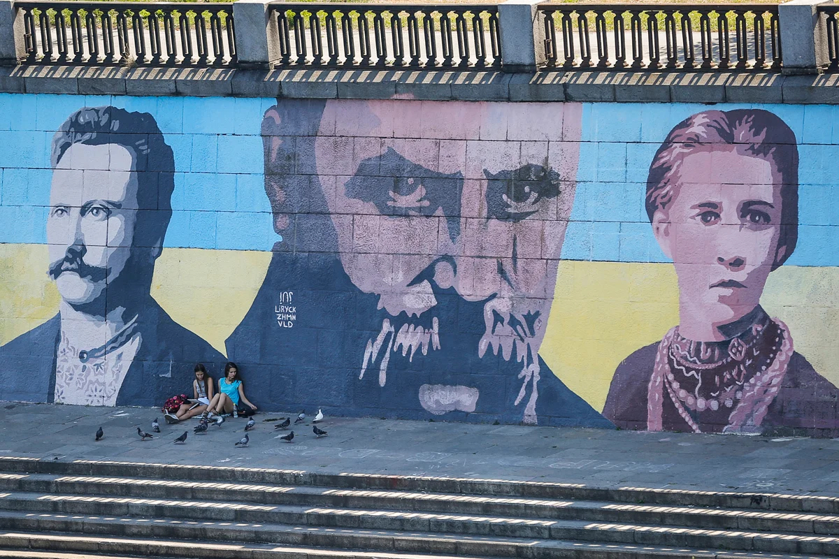 Местные жители отдыхают на фоне мурала с изображением Ивана Франко, Тараса Шевченко и Леси Украинки на набережной Днепра в Киеве, 10 августа 2015 года. Фото: Роман Пилипей / EPA