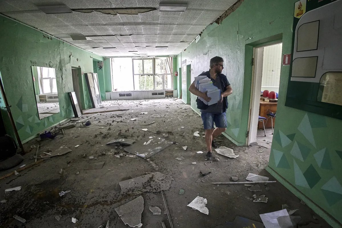 A man carrying a pile of books in a school which suffered shelling, Chuhuiv, Kharkiv region, Ukraine, 25 July 2022. Photo by Sergey Kozlov / epa.eu